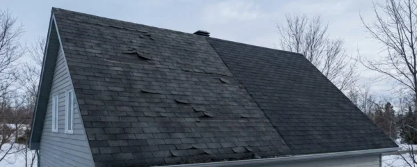 Maison suburbaine montrant une toiture en partie vieillissante avec bardeaux gondolés et gouttières obstruées.