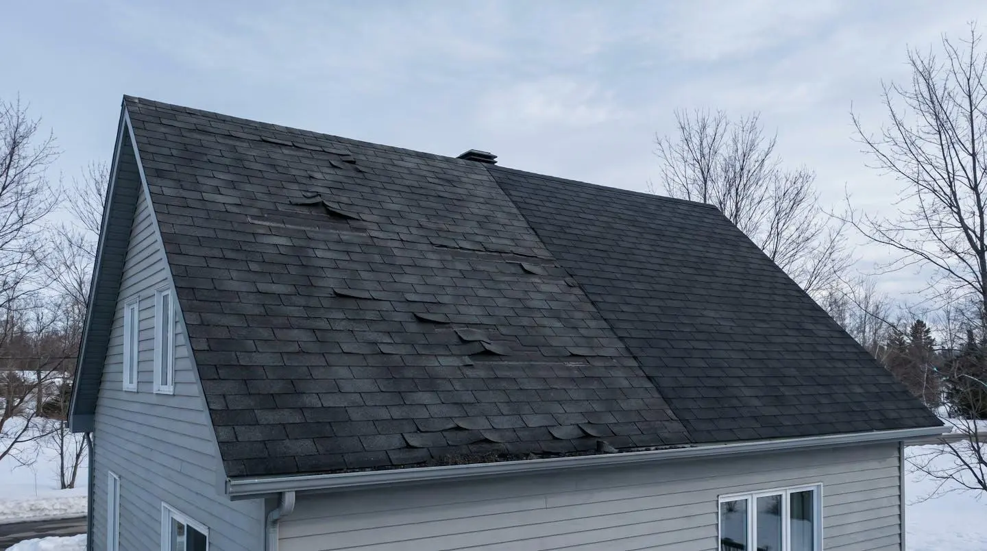 Maison suburbaine montrant une toiture en partie vieillissante avec bardeaux gondolés et gouttières obstruées.